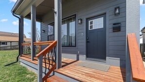 A house with a dark gray exterior, a front porch with wooden steps and a metal railing, and a dark gray door. - Renovated home minutes from downtown Indianapolis! (Indianapolis)