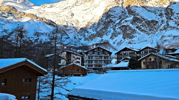 A mountain lodge with multiple wooden buildings, snow-covered surroundings, and a backdrop of snow-capped mountains. - Achat 4 by Interhome (Saas-Fee)
