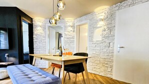 A modern living room with a dining area, stone wall, wooden flooring, and a blue sofa. - Achat 4 by Interhome (Saas-Fee)