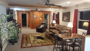 A living room with a sofa, a dining table, a ceiling fan, and a large window with curtains.