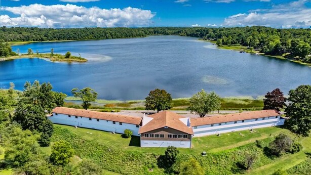 A large building with a red roof, surrounded by lush greenery and a lake.