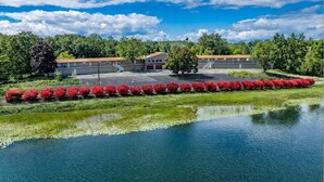 A building with a parking lot, a body of water, and red flowering plants.