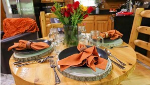 A dining table set with plates, cutlery, and napkins, with a vase of flowers in the center. - Heart Shaped Jacuzzi in main bedroom overlooking Fox Lake! Free Kayaks & Bikes (Angola)