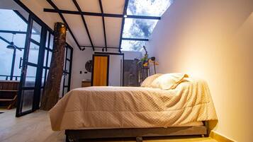 Un dormitorio con cama, un ventanal grande y el tronco de un árbol en la esquina.