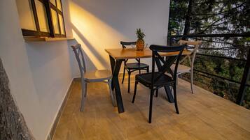 A dining area with a wooden table and chairs, a pineapple on the table, and a view of trees through a railing.