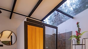 A modern bathroom with a wooden door, a glass shower enclosure, a round mirror, and a wooden vanity. - Sunrise Mountain Cabin with beautiful view and Jacuzzi, Pet friendly (Versalles)