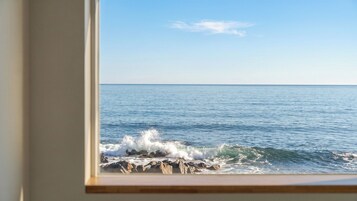 Vista del océano a través de una ventana, con olas rompiendo contra las rocas.