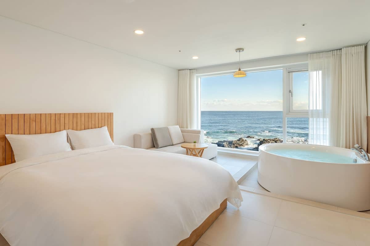 A modern bedroom with a large bed, a sofa, a small table, and a bathtub.
