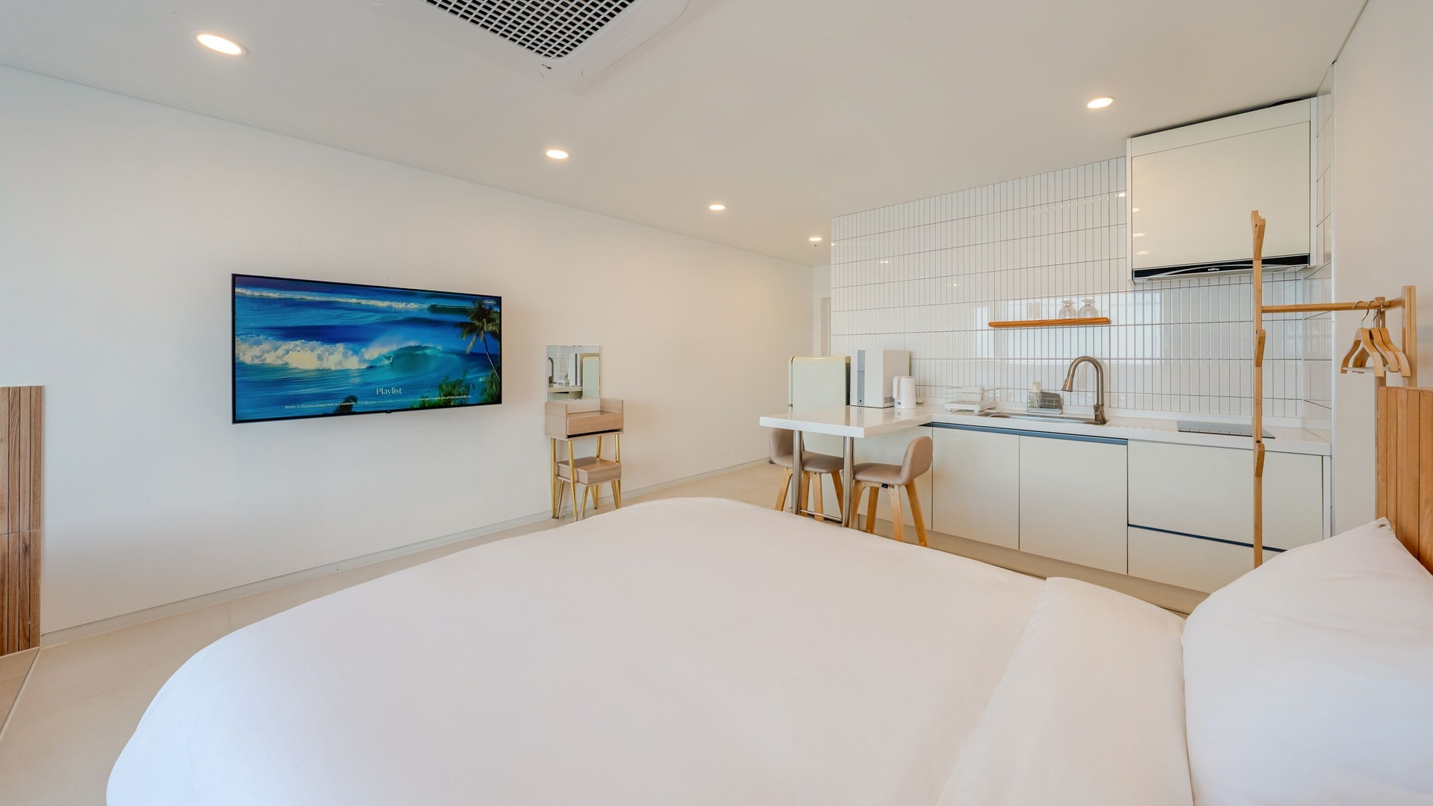 Une chambre d’hôtel moderne dotée d’un grand lit, d’un bureau avec une chaise, d’un coin cuisine avec un évier et d’une grande fenêtre.