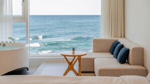 A room with a view of the ocean, a bathtub, a sofa with cushions, and a small round table. - Donghae Badadam Ocean View Spa Pension (Donghae)
