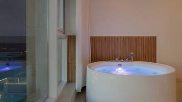 A modern bathroom with a large bathtub, a wooden panel wall, and a glass window overlooking a pool.
