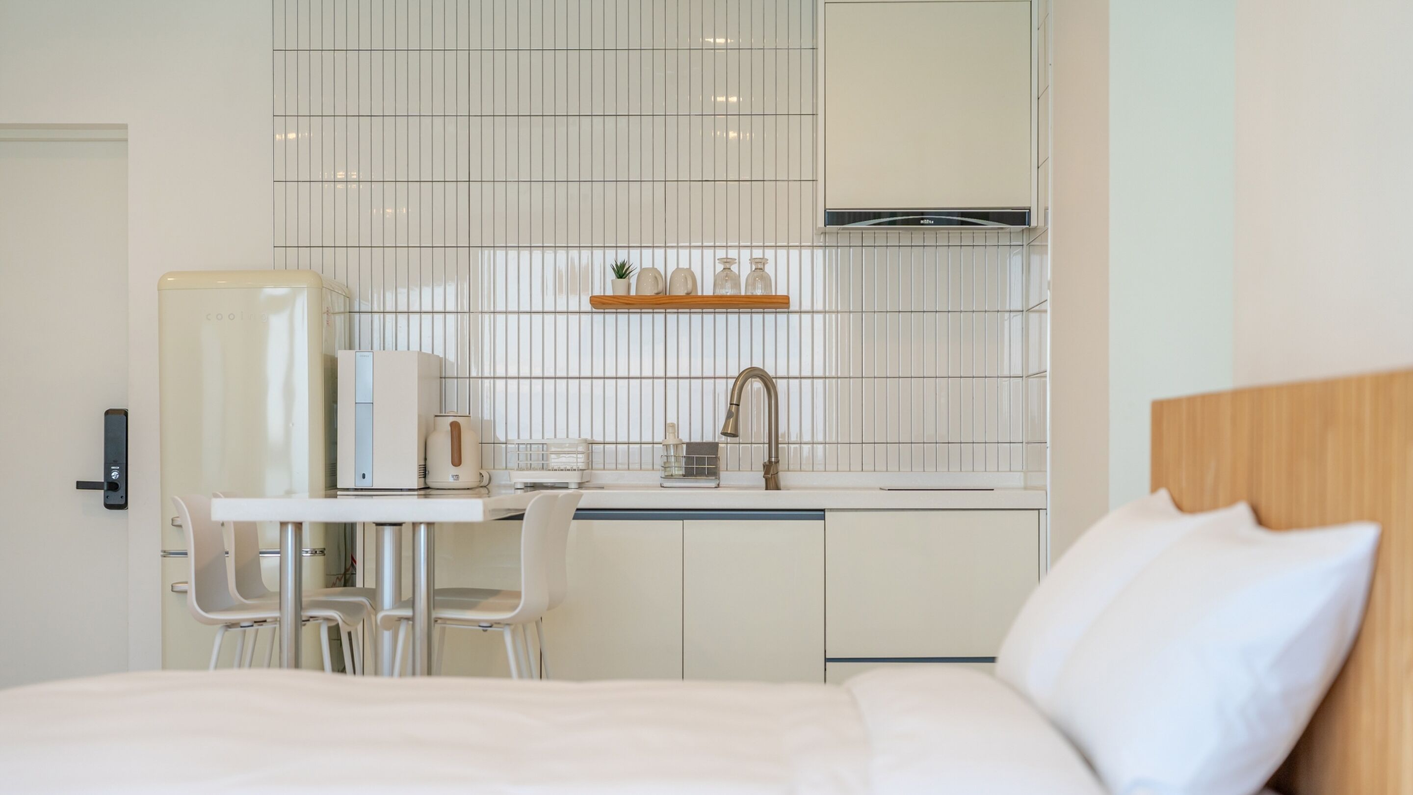 Una habitación de hotel moderna con una cama, un escritorio pequeño con una tetera, una cafetera y un espejo sobre otro espejo.