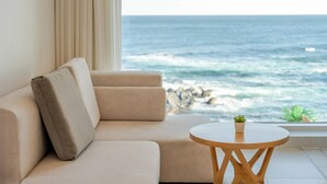 A beige sofa with cushions, a small wooden table with a plant, and a view of the ocean through a window. - Donghae Badadam Ocean View Spa Pension (Donghae)