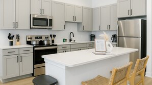 Une cuisine moderne avec des meubles gris, des appareils en acier inoxydable, un îlot central et deux chaises en osier.