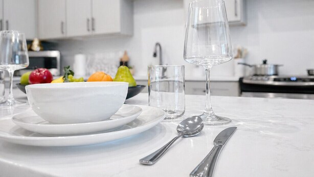 A modern kitchen with white cabinets, a marble countertop, a bowl of fruit, and dining utensils. - Cozy & Quiet Home w/ Pool, Gym, W/D WorkerFriendly (Sherman)