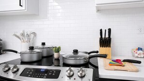 A modern kitchen with white cabinets, a stove, pots, a plant, and a cutting board. - Cozy & Quiet Home w/ Pool, Gym, W/D WorkerFriendly (Sherman)