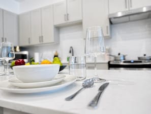 A modern kitchen with white cabinets, a marble countertop, a bowl of fruit, and a wine glass.