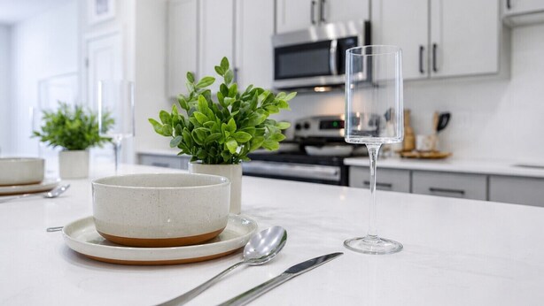 Una cocina moderna con armarios blancos, un microondas y un comedor con un tazón, cuchara, cuchillo y vaso.