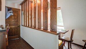 Ventana de madera con vistas a la vegetación, una puerta de madera, una silla y una pequeña mesa con un plato.