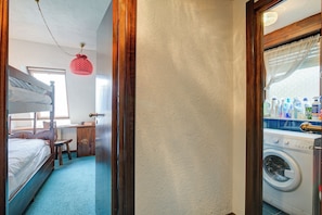 Una habitación con literas, un escritorio, una silla, una lavadora y una cesta para ropa colgada.