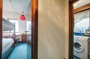 Una habitación con literas, un escritorio, una silla, una lavadora y una cesta para ropa colgada.