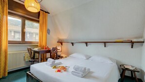 Habitación de hotel con cama, escritorio, silla, estante con libros y ventana con cortinas.