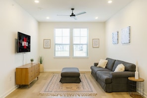A living room with a grey sofa, a wooden cabinet, a TV, and a ceiling fan. - Qeen Bed · Near Med Center · Long Worker Stays (Sherman)