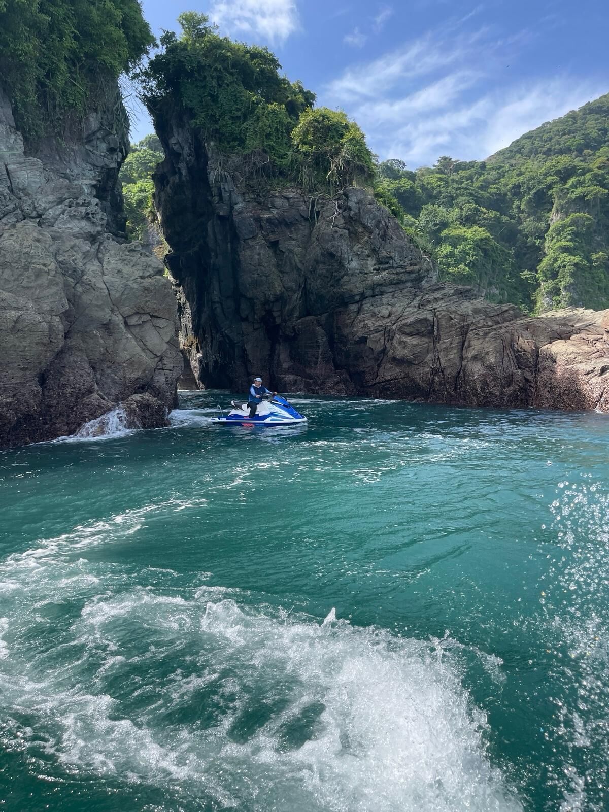 A kayaker navigating through a narrow waterway flanked by rocky cliffs and lush greenery.