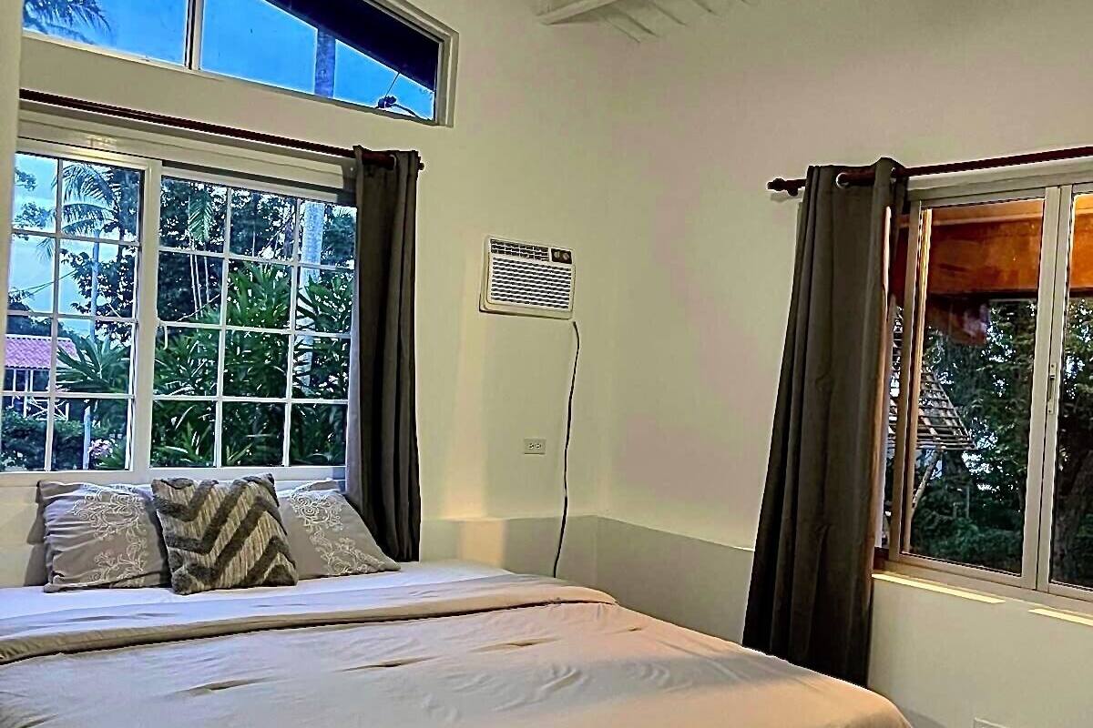 Een slaapkamer met een bed, een plafondventilator en twee ramen met gordijnen.