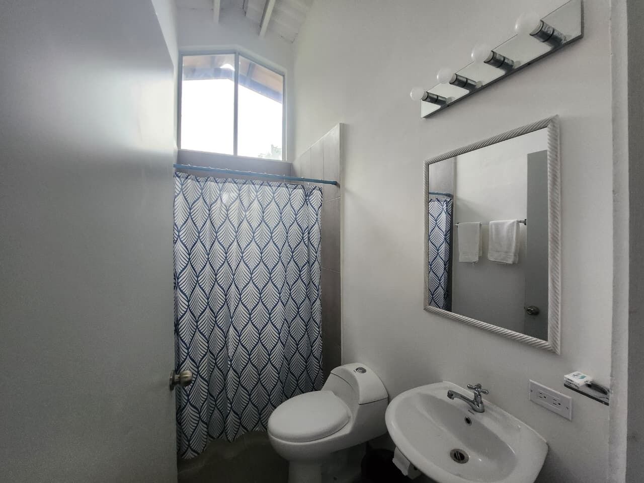 A bathroom with a patterned shower curtain, a toilet, a sink, and a mirror.