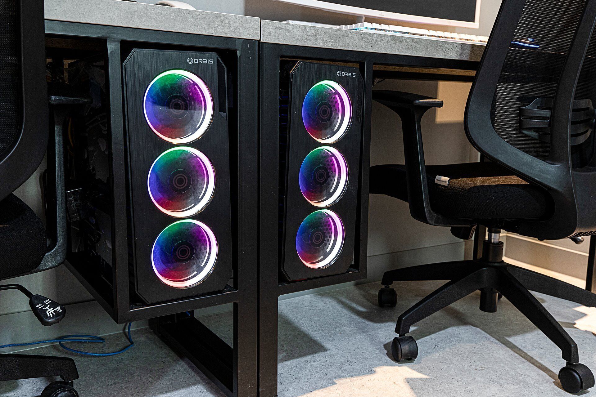 Two ORBIS computer towers with RGB lighting, a black office chair, and a desk.