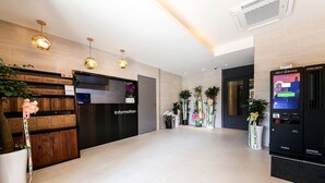 A hotel reception area with a black reception desk labeled "Information," a card deck self-service machine, and a row of potted plants. - HOTEL JUNO (Yongin)