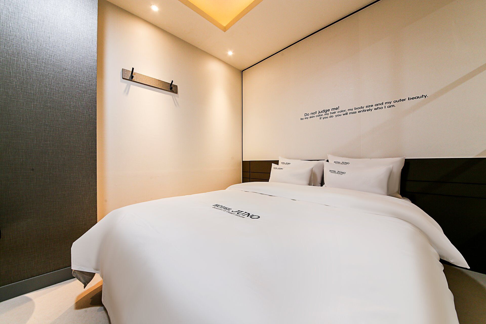 Une chambre d’hôtel moderne avec un lit bien fait, une étagère fixée au mur et une citation inspirante sur le mur.