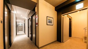 A hotel hallway with doors on both sides, a framed picture on the wall, and a coat rack in the corner. - HOTEL JUNO (Yongin)