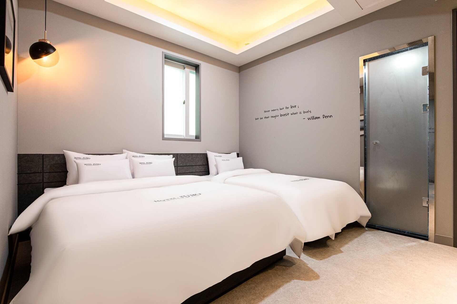 A hotel room with a modern design, featuring a large bed with white bedding, a dark headboard, and a wall-mounted light fixture.