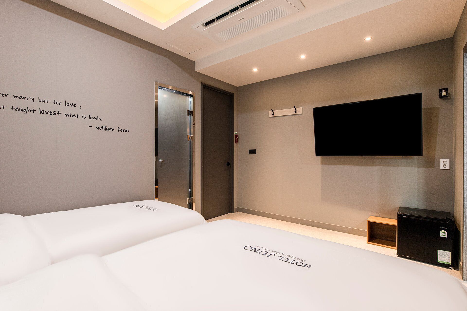 A hotel room with two beds, a mounted TV, and a note on the wall.