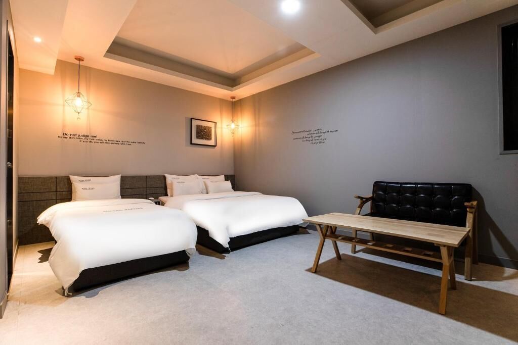 A hotel room with two beds, a wooden bench, and wall art.