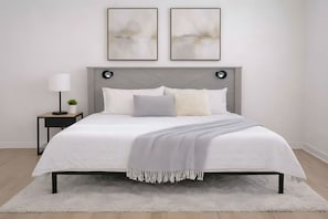Ein Schlafzimmer mit Bett, Nachttisch, Lampe und zwei abstrakten Bildern an der Wand.