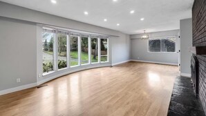 A spacious room with large windows, a wooden floor, and a fireplace.