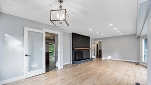 A spacious room with a wooden floor, a fireplace, and a modern chandelier.