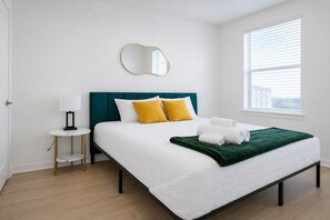 A hotel room with a bed, a bedside table, a lamp, a mirror, and a window. - Modern Stay WorkerFriendly Home w/Lndry GYM & Pool (Sherman)