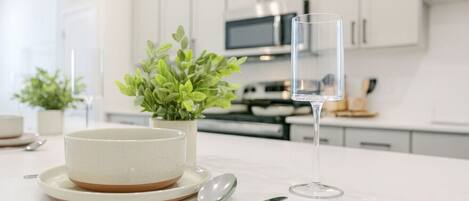 A modern kitchen with white cabinets, a microwave, and a dining table with a bowl, spoon, and glass.