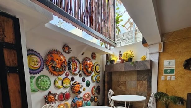 Un espace patio avec des chaises en métal blanc et une table ronde, entouré d’un mur décoré d’assiettes en céramique aux couleurs vives.