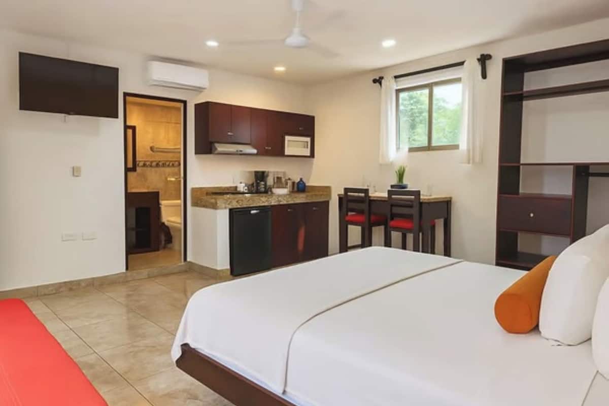 Hotelkamer met een groot bed, een bureau met stoelen, een kitchenette en een badkamer door een open deur zichtbaar.
