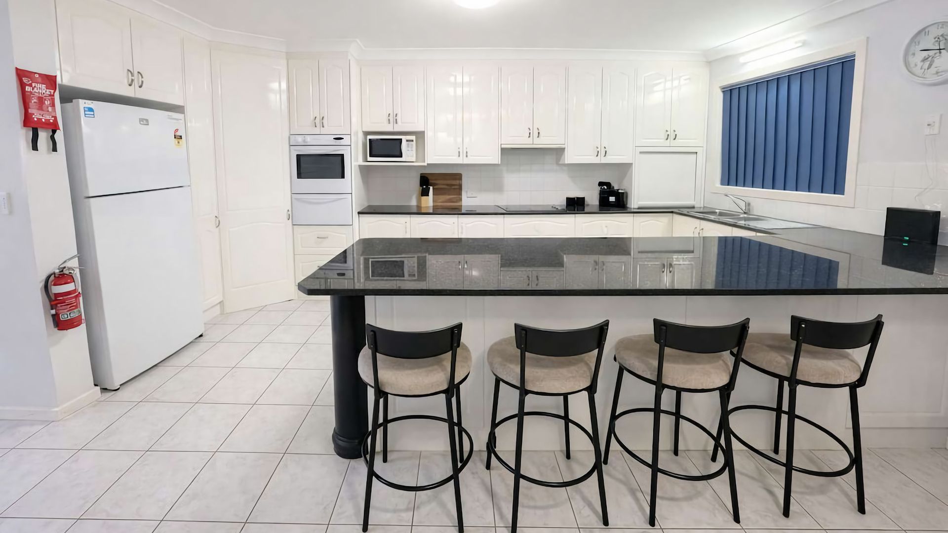 A modern kitchen with white cabinets, a black countertop, and four bar stools.