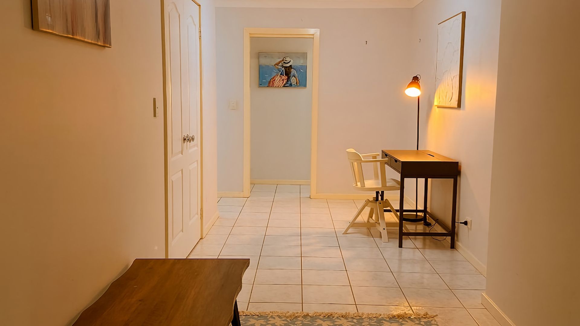 A hallway with a wooden bench, a desk with a chair, and a painting on the wall.