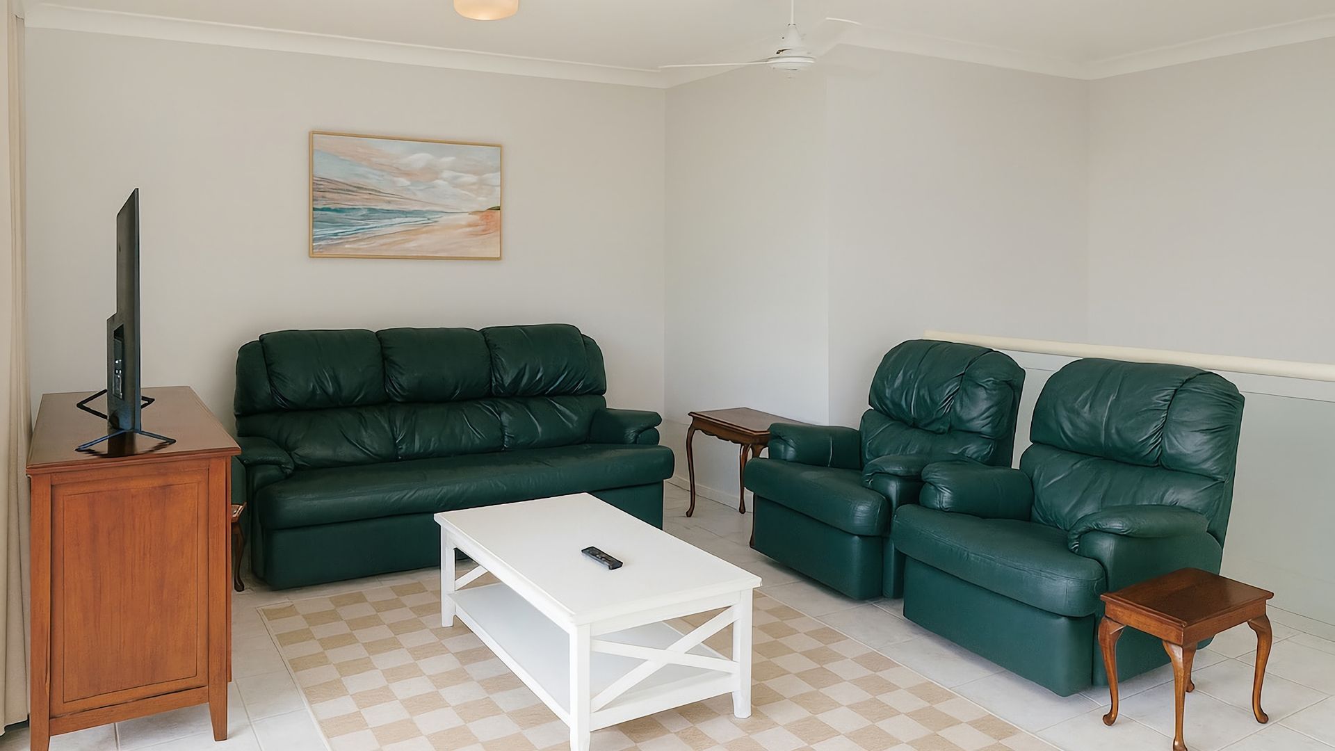 A living room with a green sofa, a white coffee table, and a television on a wooden stand.