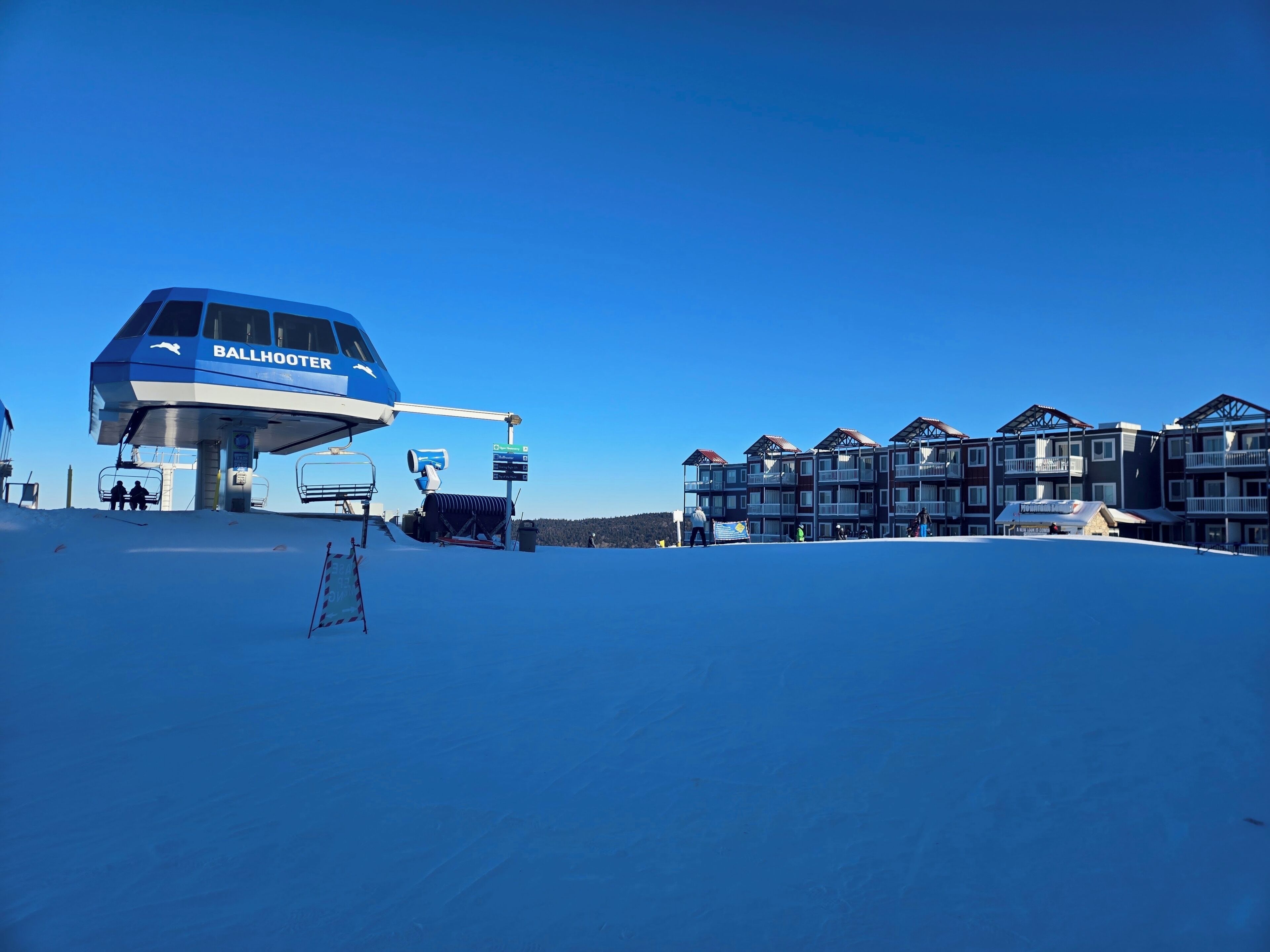 Een skibaanstation met een blauw dak en een gebouw met meerdere balkons. Op het dak staat de tekst 