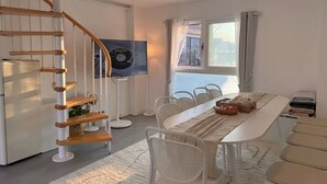 Un intérieur moderne avec un escalier en colimaçon, un coin repas avec des chaises blanches, une longue table et une vue par la fenêtre.