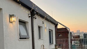 Une terrasse sur le toit, avec une table et des chaises, des guirlandes lumineuses et une vue sur le paysage urbain.